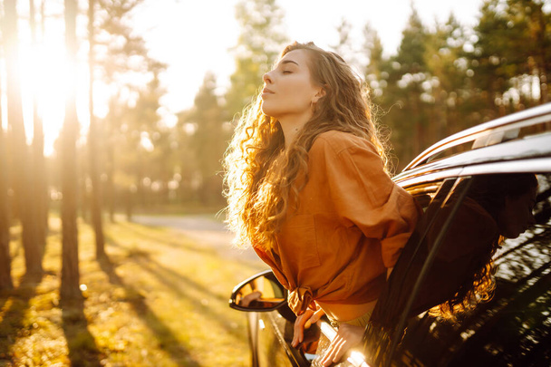 Happy curly woman smiling and enjoying nature leaning out of the car window. Feeling of freedom on the open road. Beauty and travel concept. Active lifestyle. - Photo, image