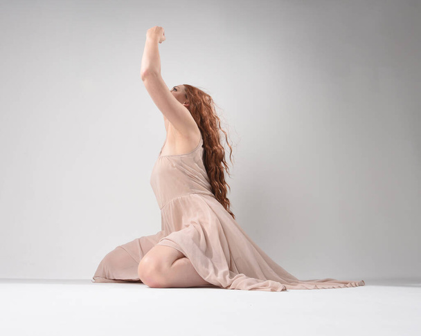 Πλήρες πορτρέτο του όμορφου μελαχρινού μοντέλου που φοράει ένα ροζ φόρεμα. χαριτωμένη στάση καθιστή, γονατιστή στα χέρια της χειρονομίας. τραβηγμένο από χαμηλή γωνία, απομονωμένο σε λευκό φόντο στούντιο. - Φωτογραφία, εικόνα