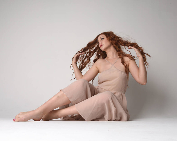 Portrait pleine longueur d'une belle mannequin brune portant une robe rose. pose assise gracieuse, agenouillée sur le sol mains gestuelles. prise de vue en angle bas, isolée sur fond de studio blanc. - Photo, image