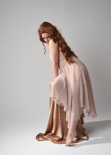 Retrato de comprimento total de belo modelo feminino com cabelos longos morena vestindo um vestido rosa cremoso. graciosa postura sentada isolada no fundo do estúdio branco. - Foto, Imagem