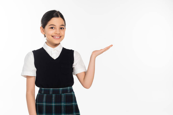 счастливая школьница, показывающая что-то рукой, указывающая и смотрящая на камеру, подающая, белая - Фото, изображение