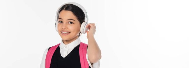 zene, vidám iskolás lány vezeték nélküli fejhallgató nézi kamera elszigetelt fehér, banner - Fotó, kép