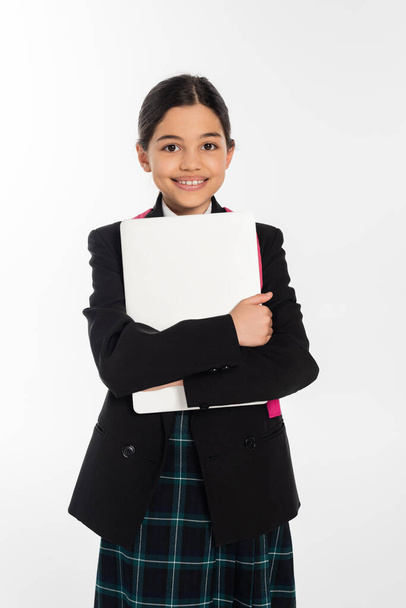 fröhliches Schulmädchen mit Laptop und Kamera, Mädchen in Schuluniform, isoliert auf weiß - Foto, Bild