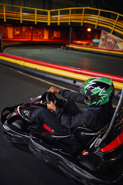 pilota afroamericano in casco che tiene il volante della macchina da corsa di karting, velocità di trasmissione - Foto, immagini