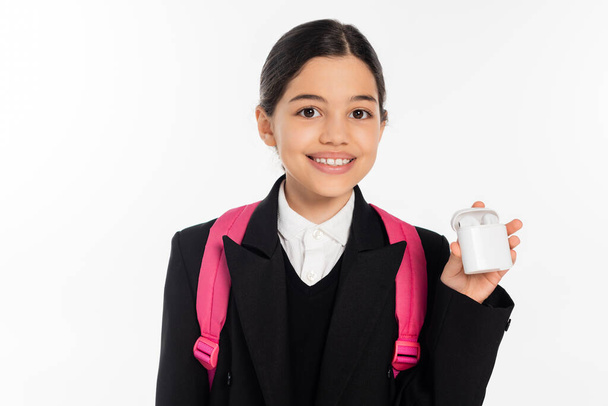 joyeuse écolière en étui de maintien uniforme avec écouteurs sans fil isolés sur blanc, positif - Photo, image