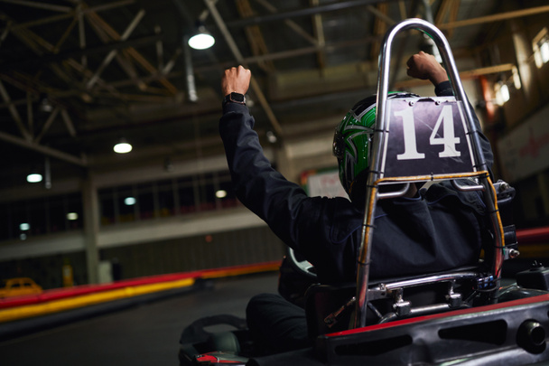 vue arrière du pilote de sport automobile en casque levant la main et gagner la course sur circuit, go-kart - Photo, image