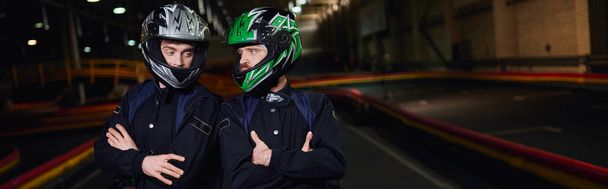 zwei selbstbewusste Kartfahrer in Sportbekleidung und Helmen, die mit verschränkten Armen auf der Strecke stehen, Banner - Foto, Bild