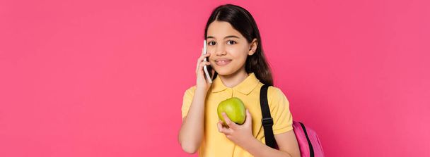 щаслива школярка стоїть з рюкзаком, тримає яблуко і розмовляє на смартфоні, телефонний дзвінок, банер - Фото, зображення