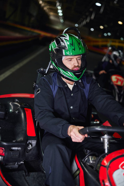 focused man in sportswear and helmet driving sport car for karting on indoor circuit, hobby - Photo, Image