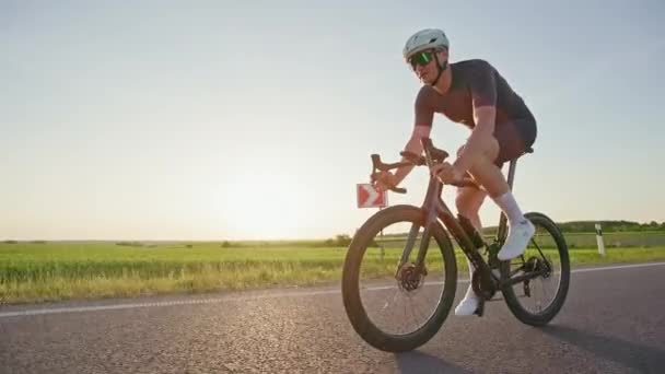 Atletische volwassene met sport gearing pedalen lichte fiets in gecontroleerd tempo bij zonsondergang. Lange afstand mannelijke fietser verbeteren van functionele fitness niveau door het doen van regelmatige training op de weg. - Video