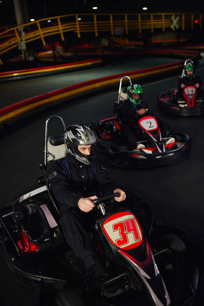 fokussiert diverse Fahrer in Helmen fahren Go-Kart auf Indoor-Rundkurs, Motorsport und Adrenalin - Foto, Bild