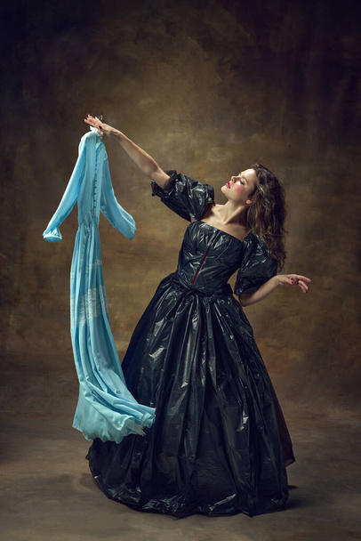 Full body portret van aantrekkelijke jonge vrouw dragen, zwarte baljurk gemaakt van vuilniszakken met blauwe midi jurk over vintage achtergrond. Concept van milieukwesties, recycling, stijl, mode. - Foto, afbeelding