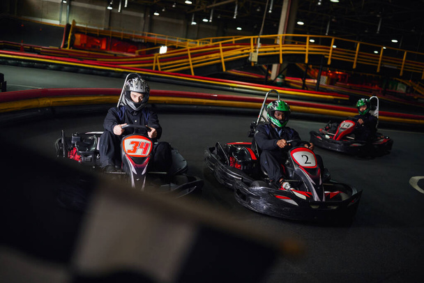 diverse men driving go kart near checkered black and white racing flag on blurred foreground - Photo, Image