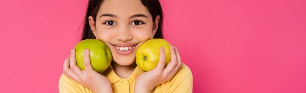 happy girl with brunette hair holding green apples on pink background, portrait, happiness, banner - Photo, Image