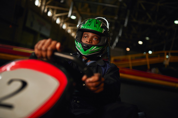 afro-americano go cart racer em capacete dirigindo no circuito indoor, speed racing challenge - Foto, Imagem