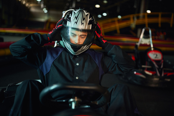 bestuurder opstijgen helm na het racen in go kart auto op circuit, snelheid rijden en motorsport concept - Foto, afbeelding