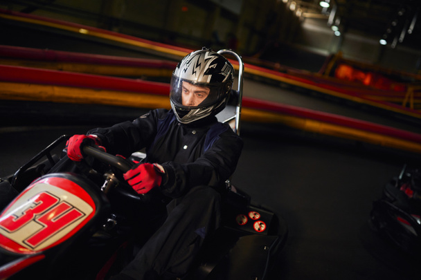 屋内サーキット,スピードドライブ,モータースポーツのコンセプトでゴーカートカーでヘルメットレーシングに焦点を当てたドライバー - 写真・画像