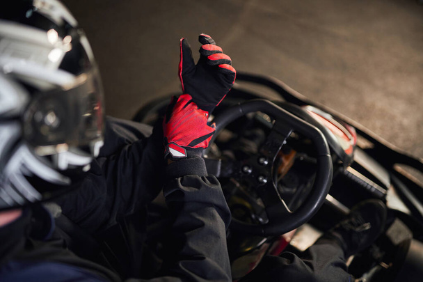 top view of go kart racer in helmet wearing red sport gloves, preparing for competition concept - Photo, Image