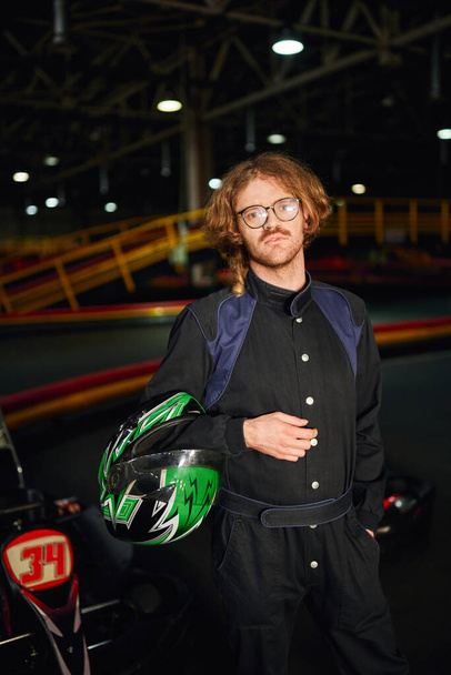go kart driver in occhiali e abbigliamento sportivo in piedi con casco all'interno di pista, circuito - Foto, immagini