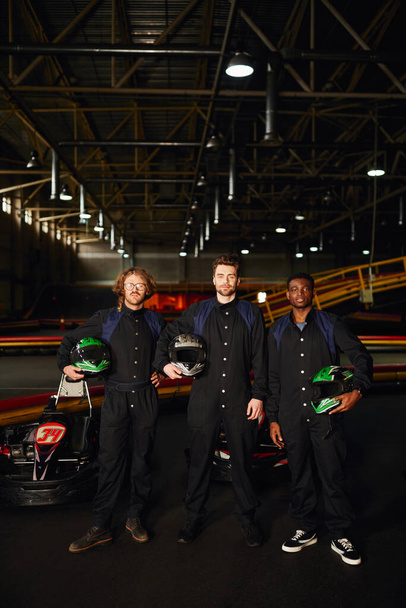 multicultural go kart drivers em ternos de proteção de pé e segurando capacetes, concorrentes - Foto, Imagem