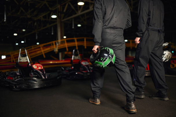 スポーツウェアでゴーカートのドライバーがサーキットを歩き,ヘルメットを保持し,競合他社を保持する見た目 - 写真・画像