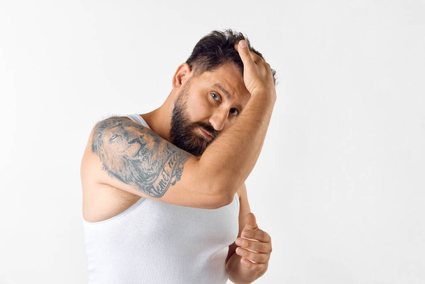 Handsome, mature, bearded man taking care after hair with cosmetics, applying hair styling gel against white background. Concept of mens beauty, skin care, cosmetology, health and wellness. - Photo, Image