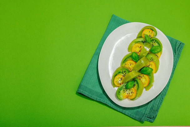 Tuore kesäsalaatti vihreästä perintökalleudesta tomaatti Kiwi, tuoreet basilikan lehdet ja ekstra-neitsytoliiviöljy. Terveellistä ruokaa konsepti, kova valo, tumma varjo. Kirkas tausta, tasainen lay, ylhäältä - Valokuva, kuva