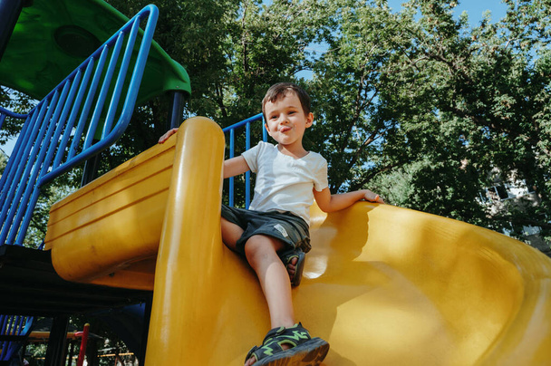 szczęśliwy dziecko przedszkole chłopiec bawiąc się na zjeżdżalni na placu zabaw w lecie - Zdjęcie, obraz