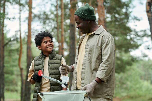 アフリカ系アメリカ人の父親が森で息子と一緒にゴミ拾い - 写真・画像