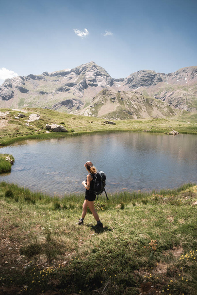 backpacker woman enjoying the landscape of a lake in the Pyrenees during a summer hiking trip in Huesca. - Фото, изображение