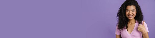 Jeune femme noire riant tout en gesticulant pouce vers le haut isolé sur fond violet - Photo, image