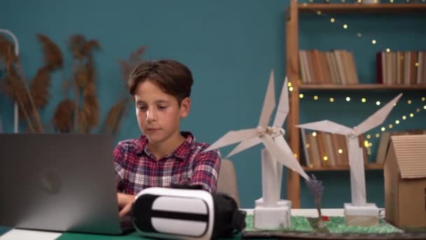 Школьник носит AR гарнитуру с помощью ноутбука, будущее, дизайн проекта ветряной турбины с домом, футуристический дизайн с технологическим применением основных. Копирование пространства - Кадры, видео