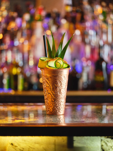 Copa de metal con refrescante cóctel con rodajas de pepino y piña servido en el mostrador en el bar moderno - Foto, Imagen