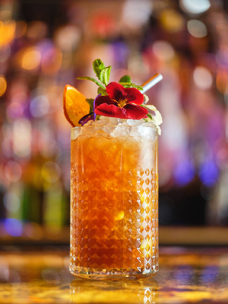 Verre de cocktail à boisson longue avec glaçons et décorations servis sur le comptoir dans un bar moderne sur fond flou avec bokeh - Photo, image