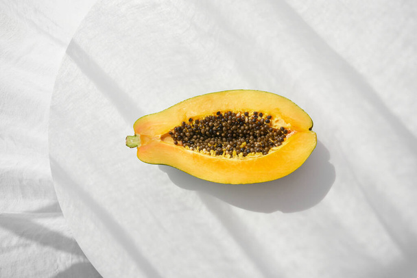 Вид сверху половины аппетитной свежей спелой папайи с семенами и апельсиновой мякотью, выставленной на стол под солнечным светом с тенью - Фото, изображение