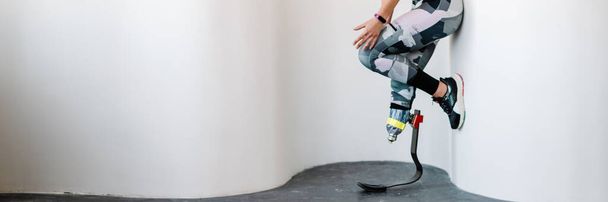 Young sportswoman with prosthesis working out by wall indoors - 写真・画像