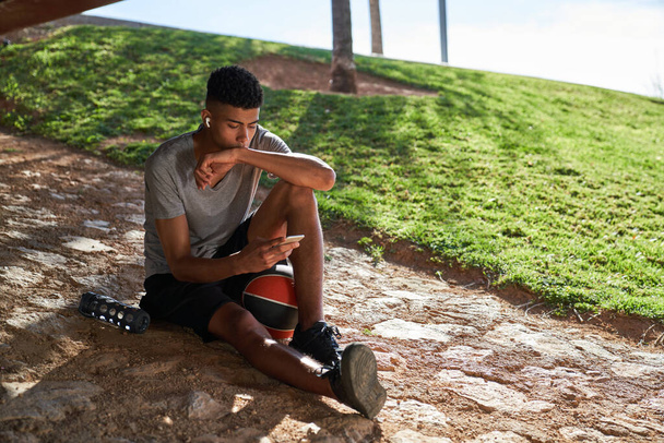 Koko kehon latino urheilullinen mies pallo kuuntelee musiikkia, kun tekstiviestit matkapuhelin o street of city - Valokuva, kuva