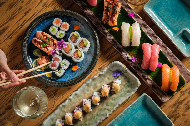 Vista superior de la persona anónima de la cosecha con palillos comiendo sabroso rollo de sushi con atún crudo en la mesa servida con vaso de vino blanco - Foto, imagen