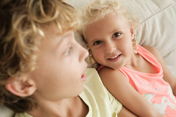 High angle of cute preteen sister with curly blond hair spending time with elderly brother on couch - Photo, Image