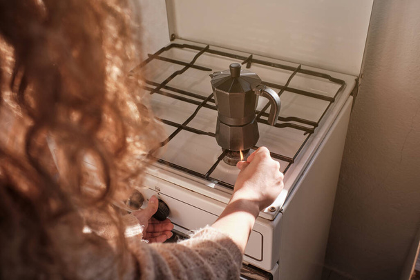 Van boven van gewas anonieme vrouw met krullend haar verlichting gasfornuis tijdens het bereiden van koffie in metalen geiser koffiezetapparaat in de keuken - Foto, afbeelding
