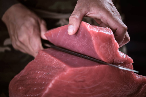 Mains masculines d'un chef coupant une délicieuse longe de thon rouge frais. - Photo, image