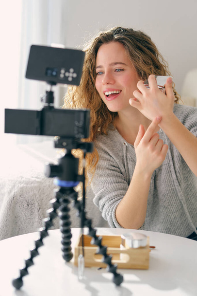 Bloggerin zeigt Hand mit feuchtigkeitsspendender Creme, während sie Make-up-Tutorial für professionelle Kamera zu Hause ausstrahlt - Foto, Bild