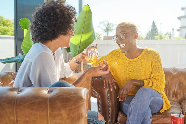 Femme afro-américaine positive parlant avec un ami assis sur le canapé à la maison pendant le week-end - Photo, image