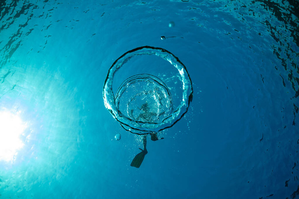 Draufsicht auf unkenntliche männliche Touristen in Schwimmflossen, die an sonnigen Tagen unter transparentem, blauem Wasser mit Blasen schwimmen - Foto, Bild