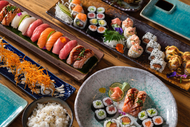 Van boven verschillende smakelijke sushi en broodjes met verse vis geserveerd op bord en dienbladen op houten tafel met rijstkom - Foto, afbeelding