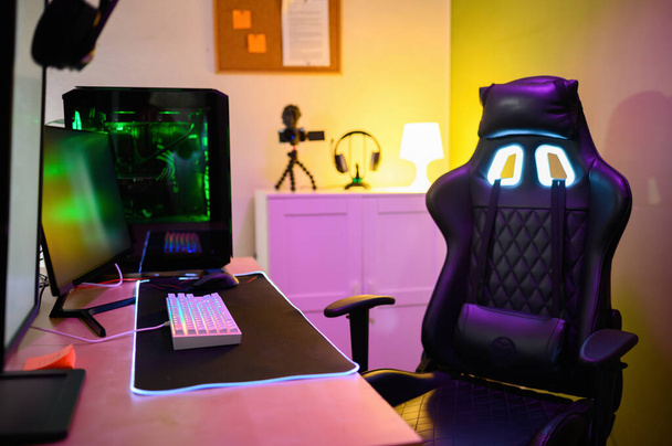 Modern gadgets computer monitor connected keyboard neon lights gaming PC video camera headphones and cozy headrest armchair placed in illuminated room - Photo, Image