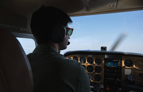 Visão traseira aviador masculino focado em fones de ouvido e óculos de sol voando helicóptero moderno em céus azuis sem nuvens - Foto, Imagem