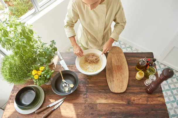 De cima mulher de cultura em ingredientes de mistura uniformes para bife tartare em placa de cerâmica branca enquanto cozinha - Foto, Imagem