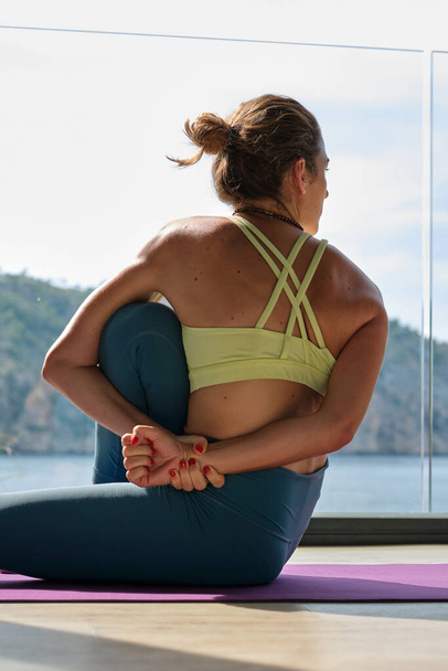 Baixo ângulo de fêmea flexível em sportswear fazendo ioga em Sage Marichi posar enquanto sentado no tapete no terraço no verão - Foto, Imagem