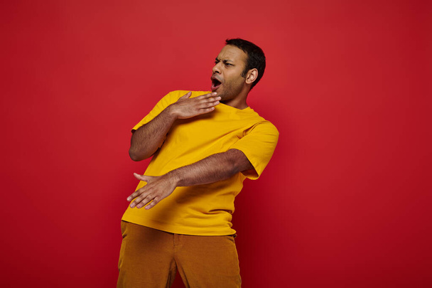 emotionaalinen intialainen mies kirkkaissa rento vaatteet osoittavat ilmeikäs reaktio punaisella taustalla, wow - Valokuva, kuva